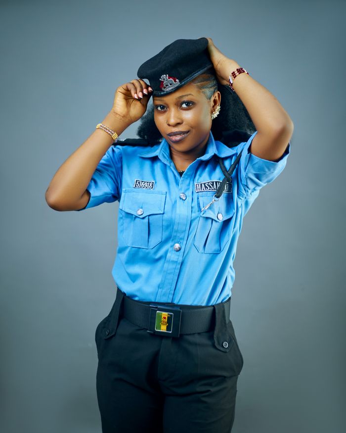 services-04 Portrait of a female police officer adjusting her cap, wearing a blue uniform against a neutral background.