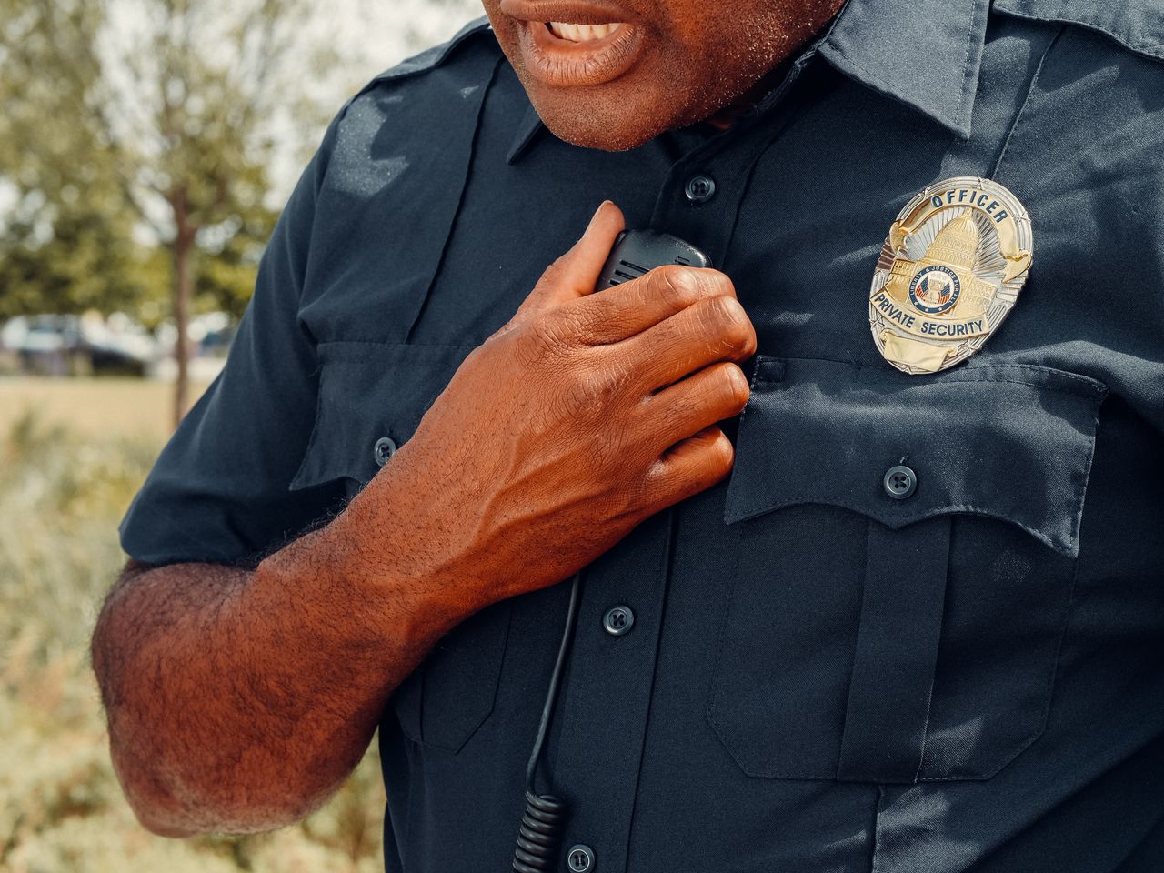 who-we-are Close-up of a security officer using a radio outdoors, showcasing professional security attire.