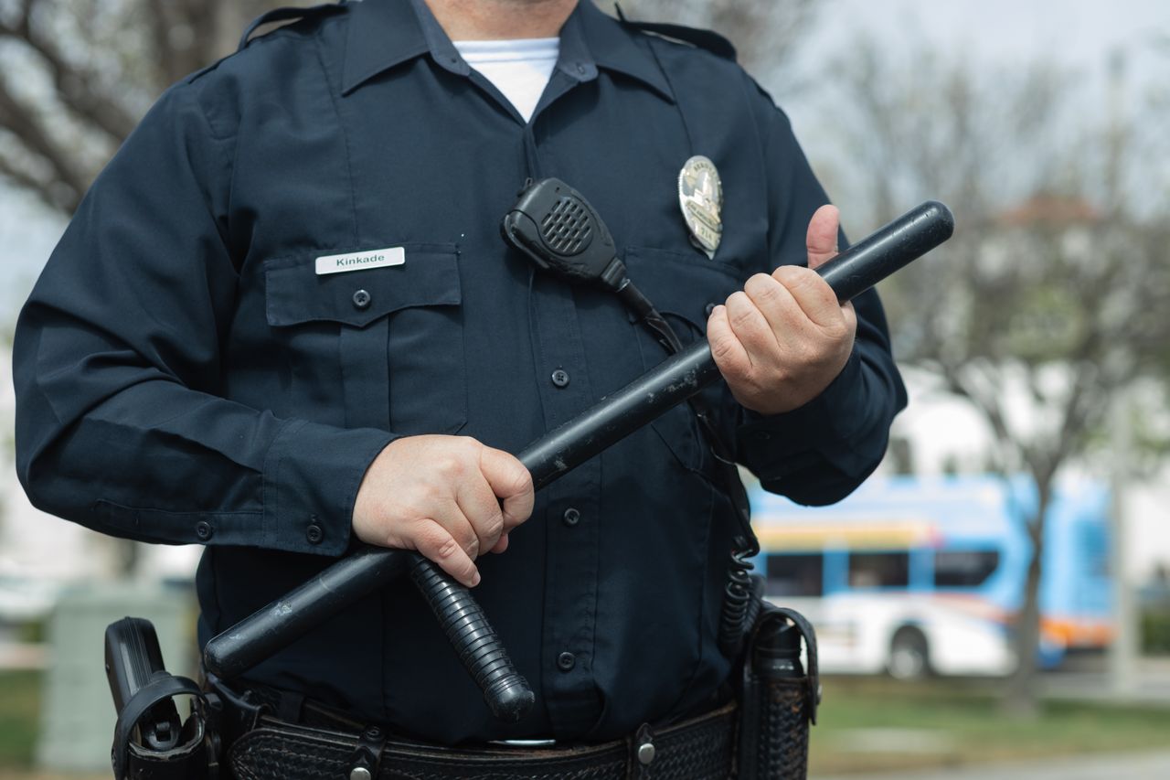 services-03 Close-up of a police officer holding a baton outdoors, emphasizing authority and security.